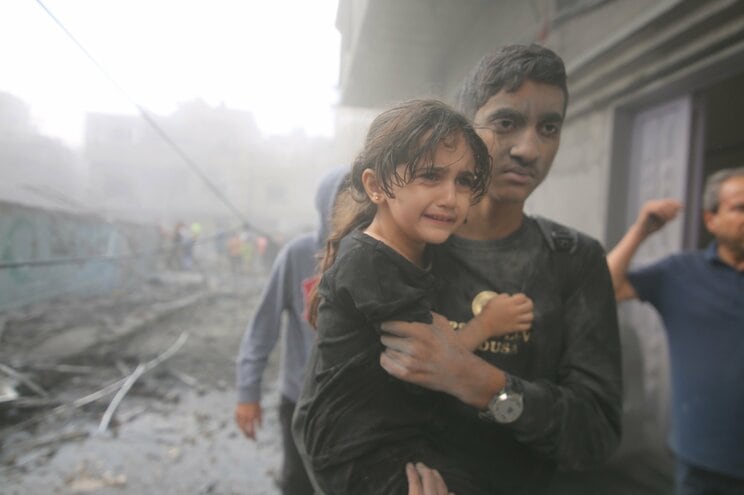 10月12日、ガザ地区南部の都市ラファで、イスラエル軍の空爆で破壊された建物から少女を抱えて避難する男性　写真／新華社・共同通信イメージズ
