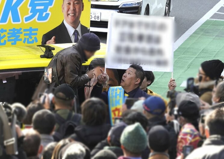 演台に上がって立花孝志氏と罵り合う抗議者の男性。後ろのプラカードを立花陣営関係者に持たせている（撮影／集英社オンライン）