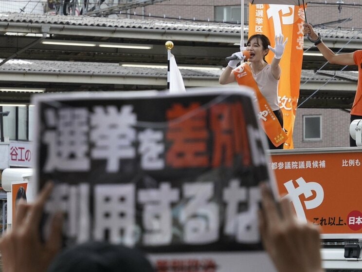 7月13日、成増駅前で演説するさや氏と参政党の公約に抗議するプラカード（撮影／集英社オンライン）