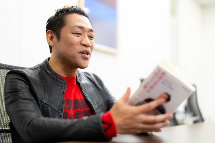 著書を見つめながら優しく笑うはなわ　撮影／佐藤靖彦