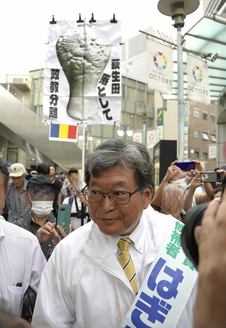 10月19日、JR八王子駅前で萩生田光一氏の背後に現れた、萩生田氏を非難するプラカード(撮影/集英社オンライン)