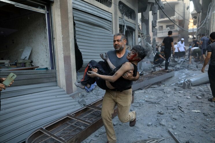 10月19日、ガザ地区南部の都市カーンユニスでイスラエルによる空爆後、負傷した子供を移送する男性　写真／Yasser Qudih・新華社・共同通信