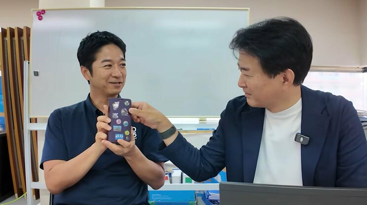 柳ヶ瀬氏に、高市首相らのシールを貼ったスマホを見せる藤田氏（画像／公式YouTube動画より）