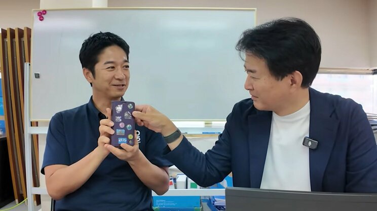 柳ヶ瀬氏に、高市首相らのシールを貼ったスマホを見せる藤田氏（画像／公式YouTube動画より）