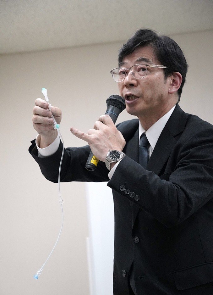 犯行に使われたのと同じ点滴用の延長チューブを示す柏たなか病院の長谷川奉延病院長。長さ約55センチのチューブのうち、小指で差した青い突起がある「側管」と呼ばれる部分から注射器で大便をチューブに混入させたとし、そこから下端までが茶色く変色していたという（撮影／集英社オンライン）