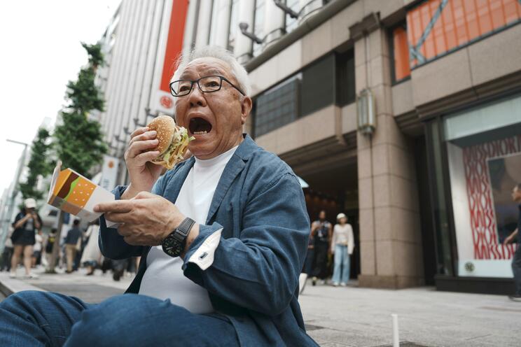 １号店があった三越前の歩道で、ビッグマックにかぶりつく山迫さん〈読売新聞提供〉